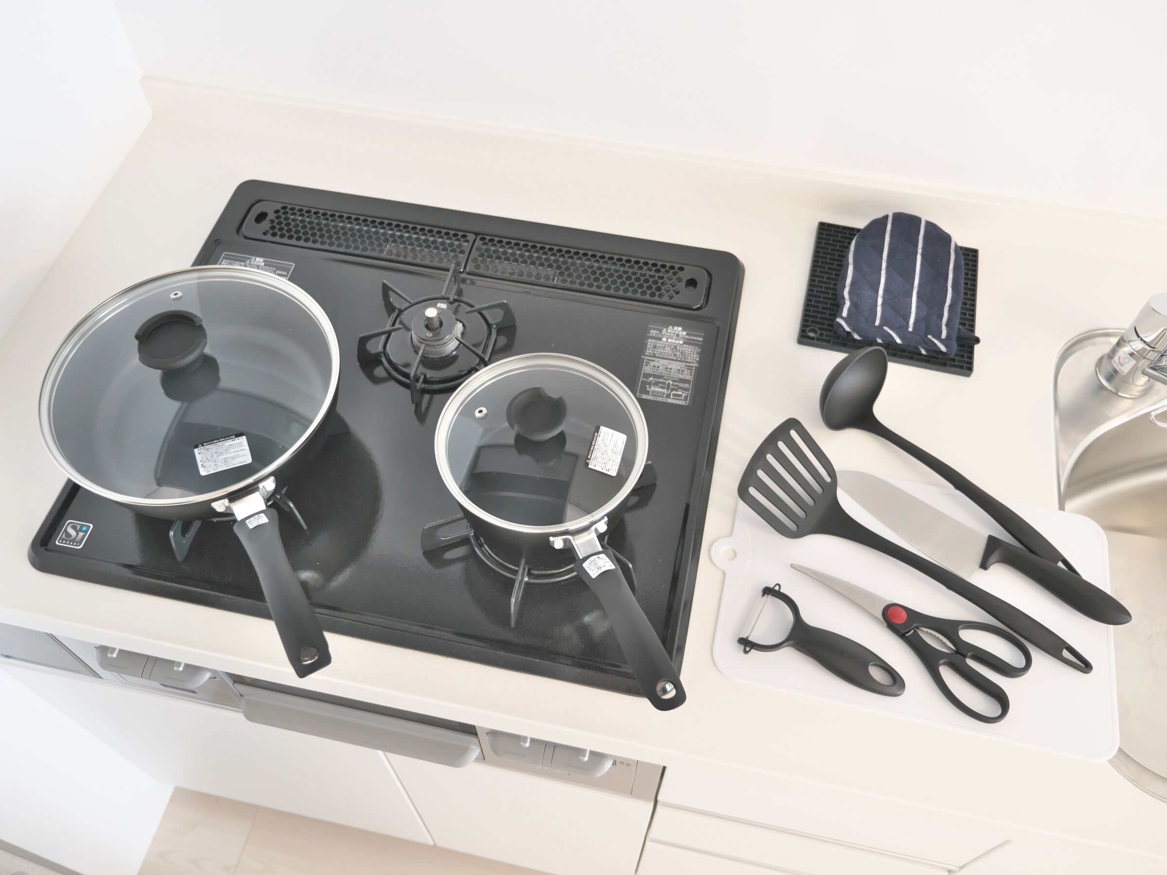 A kitchen with a stove, pots, a spatula, and a pair of scissors.