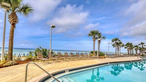 A poolside area with lounge chairs, palm trees, and a view of the ocean. - Calypso Resort by BBG (Panama City Beach)