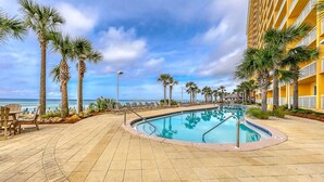 A pool area with a clear view of the ocean, surrounded by palm trees and lounge chairs. - Calypso Resort by BBG (Panama City Beach)