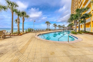 A pool area with a clear view of the ocean, surrounded by palm trees and lounge chairs. - Calypso Resort by BBG (Panama City Beach)