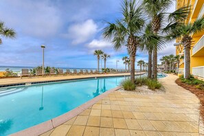 A pool area with a clear view of the ocean, surrounded by palm trees and a yellow building. - Calypso Resort by BBG (Panama City Beach)