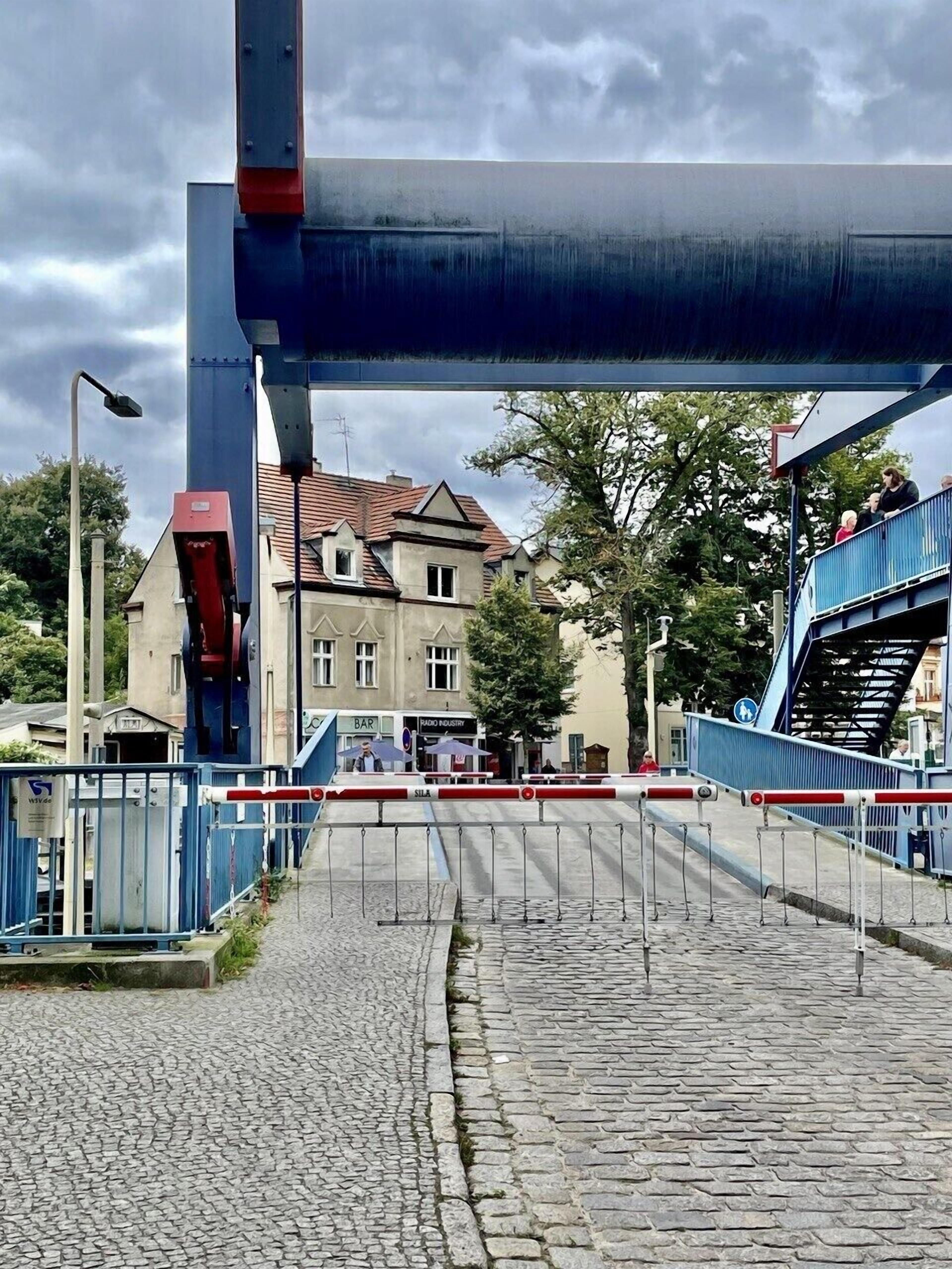 A cobblestone street under a bridge with a building and a bar in the background.