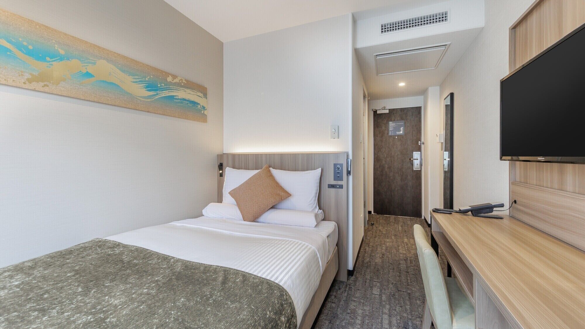 A hotel room with a bed, a desk, a television, and a painting on the wall.