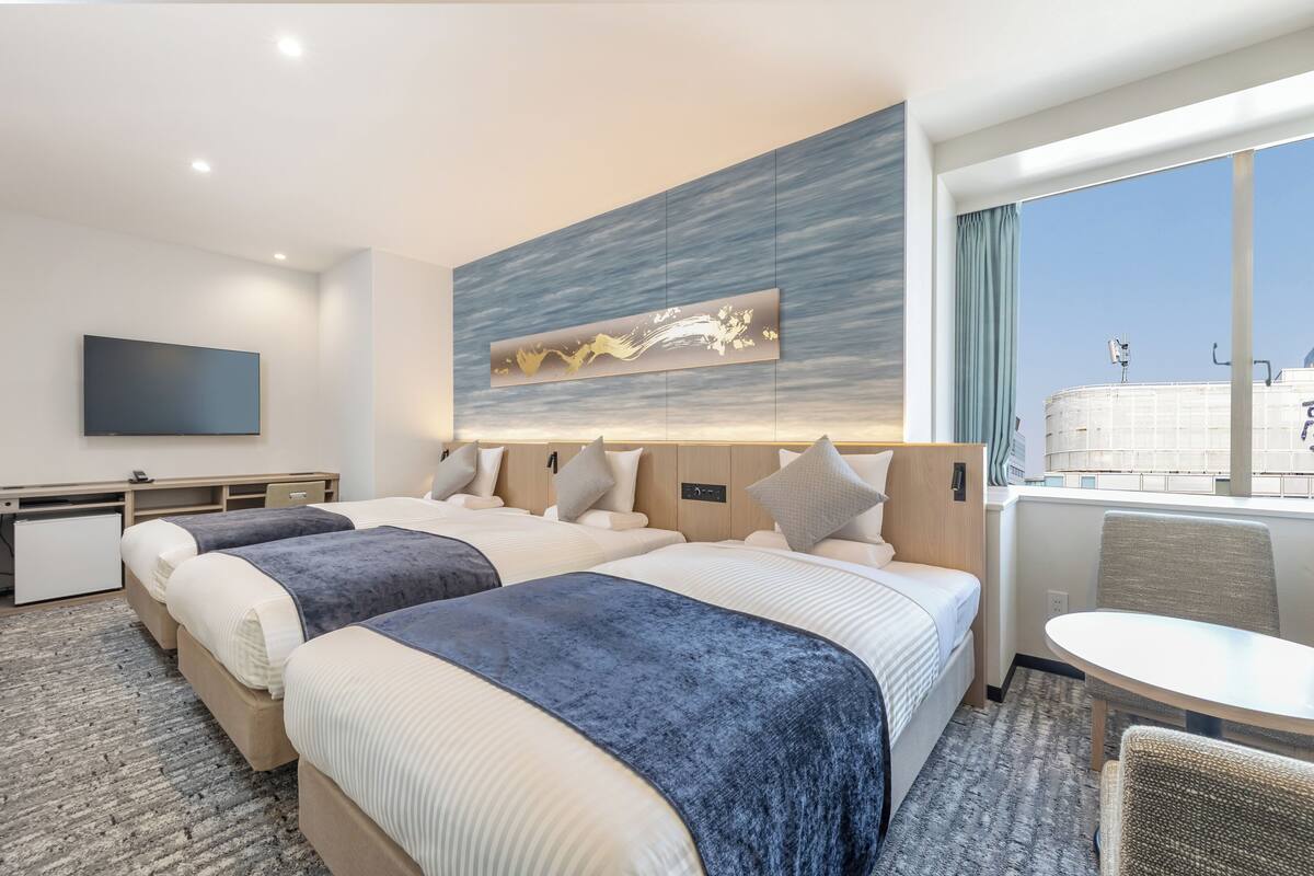 A hotel room with two beds, a desk, a chair, and a large window with a view.