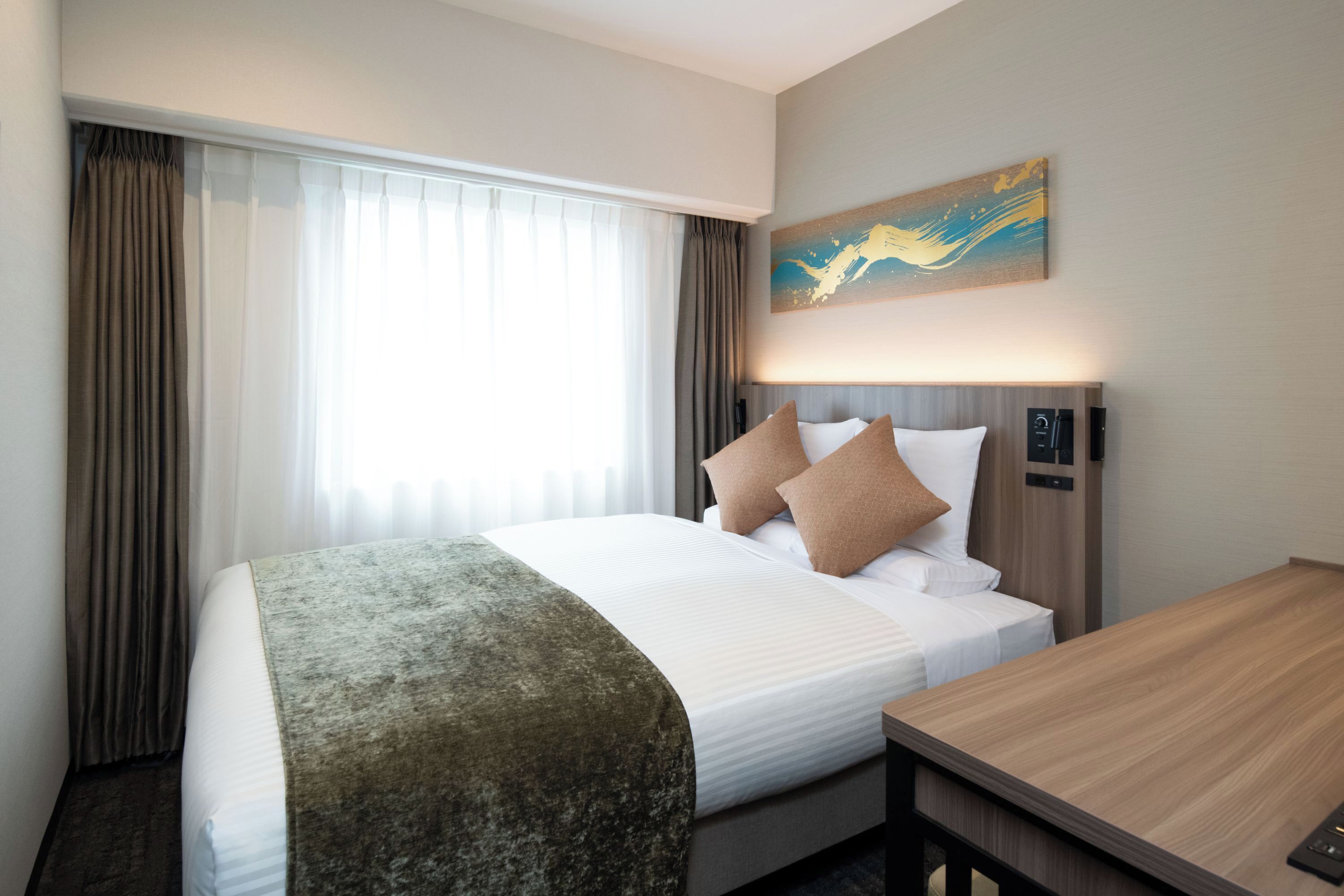 A hotel room with a large bed, a wooden desk, and a painting on the wall.