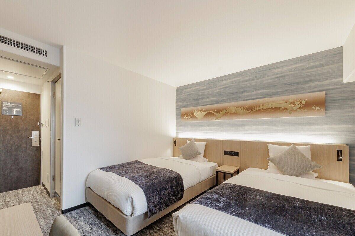 A hotel room with two beds, a desk, and a modern wall art piece.