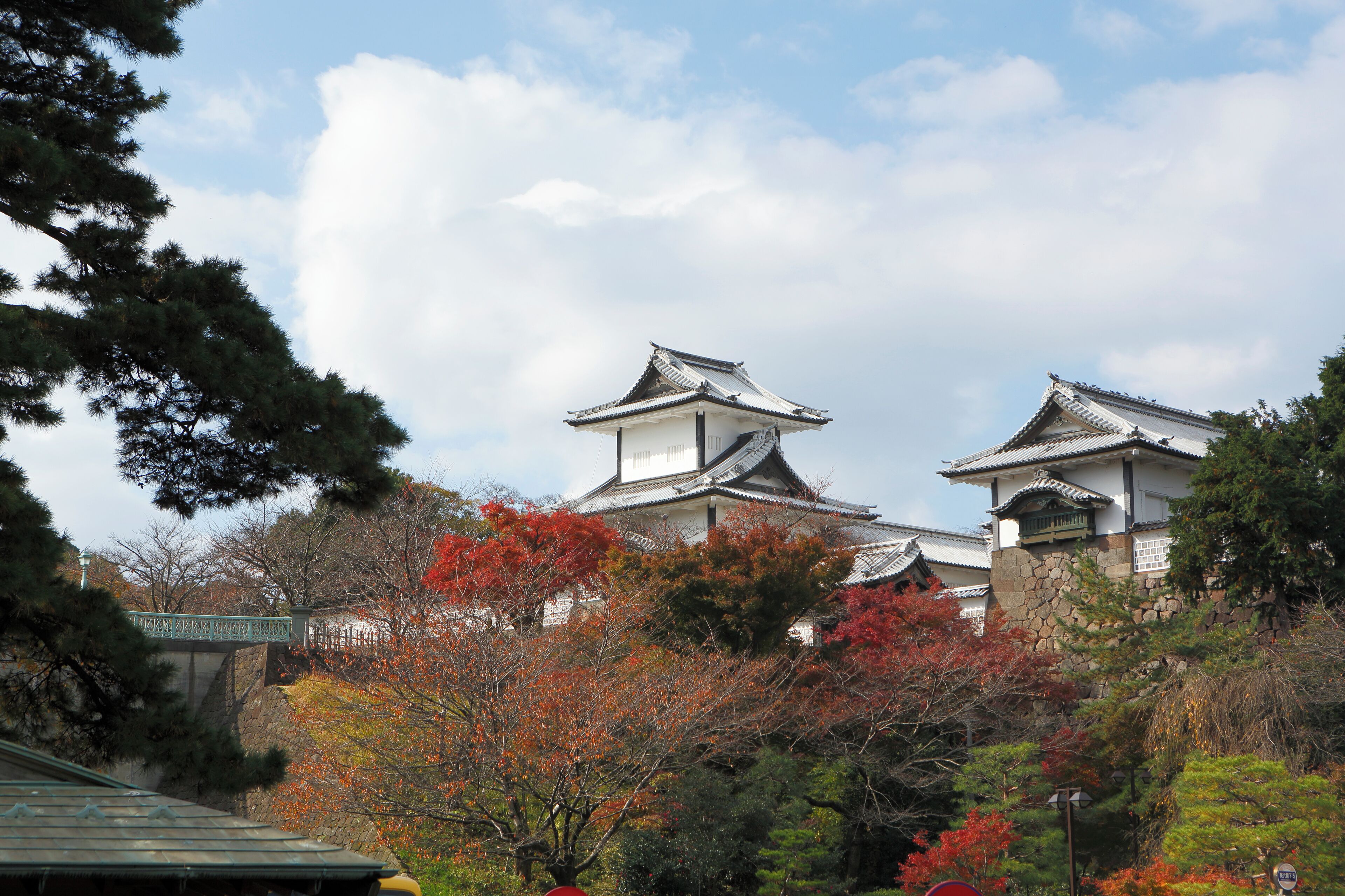 Un edificio tradicional japonés con tejado de tejas y paredes blancas, rodeado de follaje otoñal.
