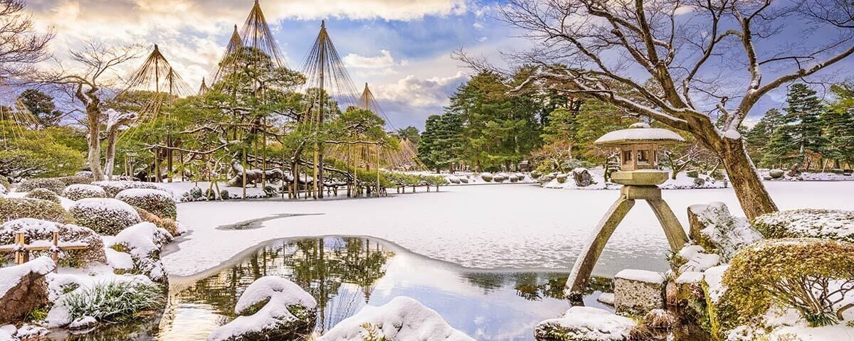 A serene winter garden with a pond, snow-covered trees, and traditional Japanese structures.