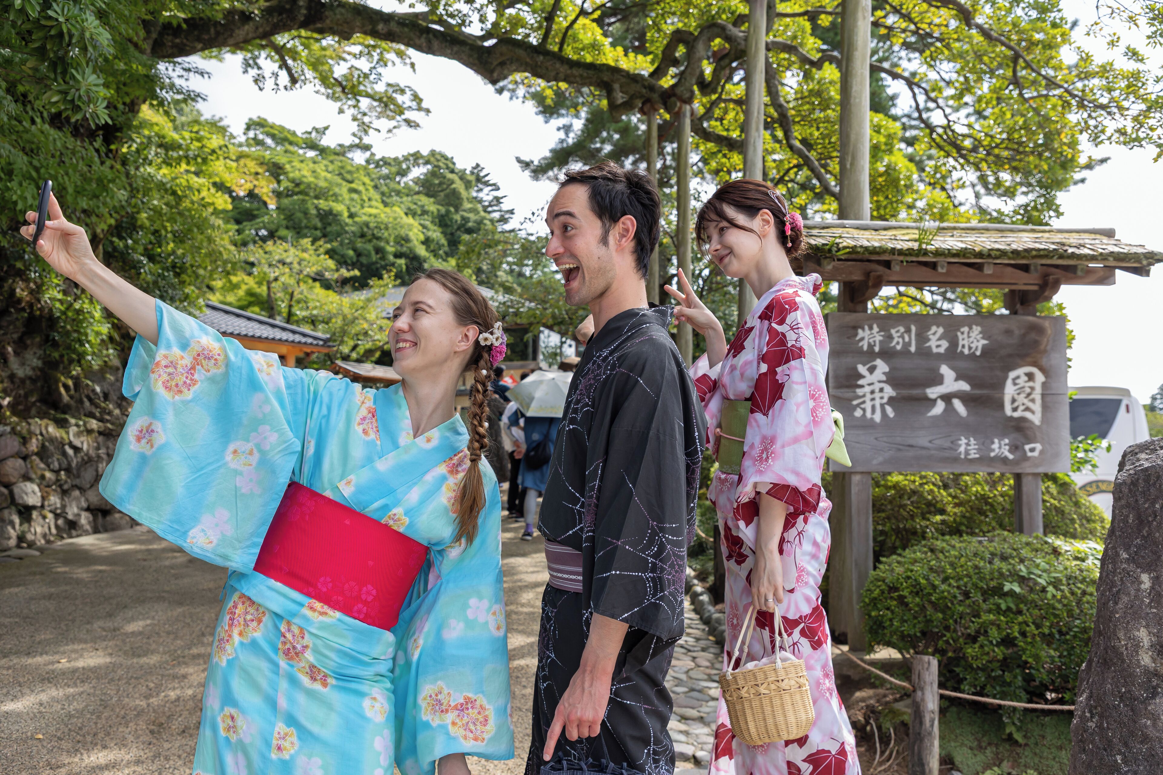 Un entorno japonés tradicional con personas vestidas con kimonos, un sendero de piedra y un letrero con caracteres japoneses.