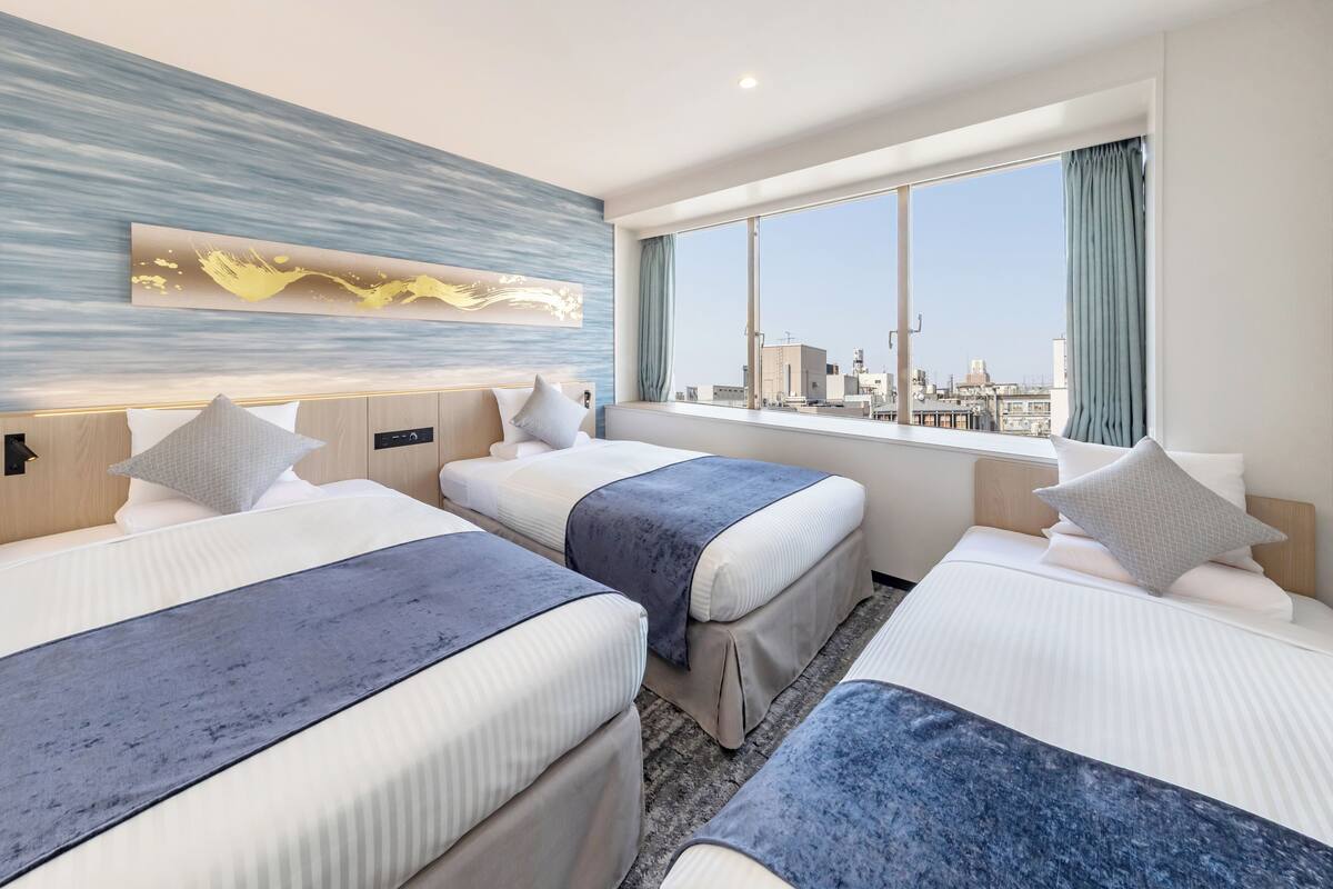 A hotel room with two beds, a large window with a city view, and a modern abstract painting on the wall.