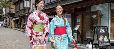 Two individuals in traditional attire walking on a street with wooden buildings and a signboard.