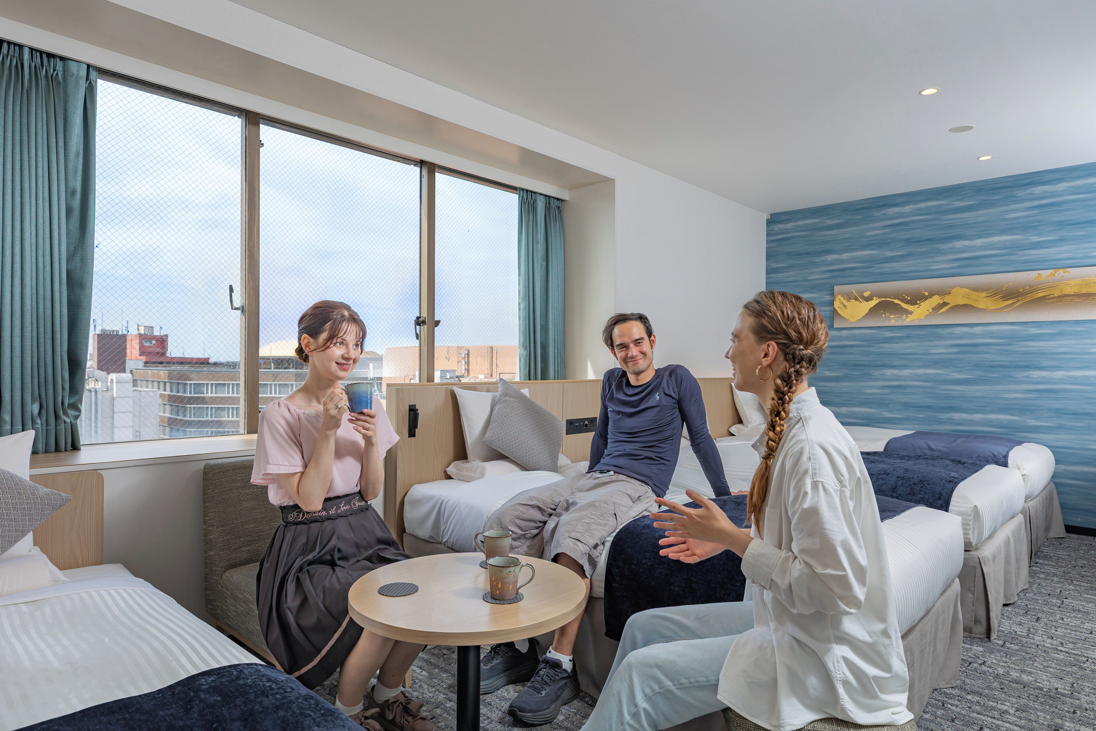 A hotel room with a large window, a bed, a sofa, and a small table with a cup.