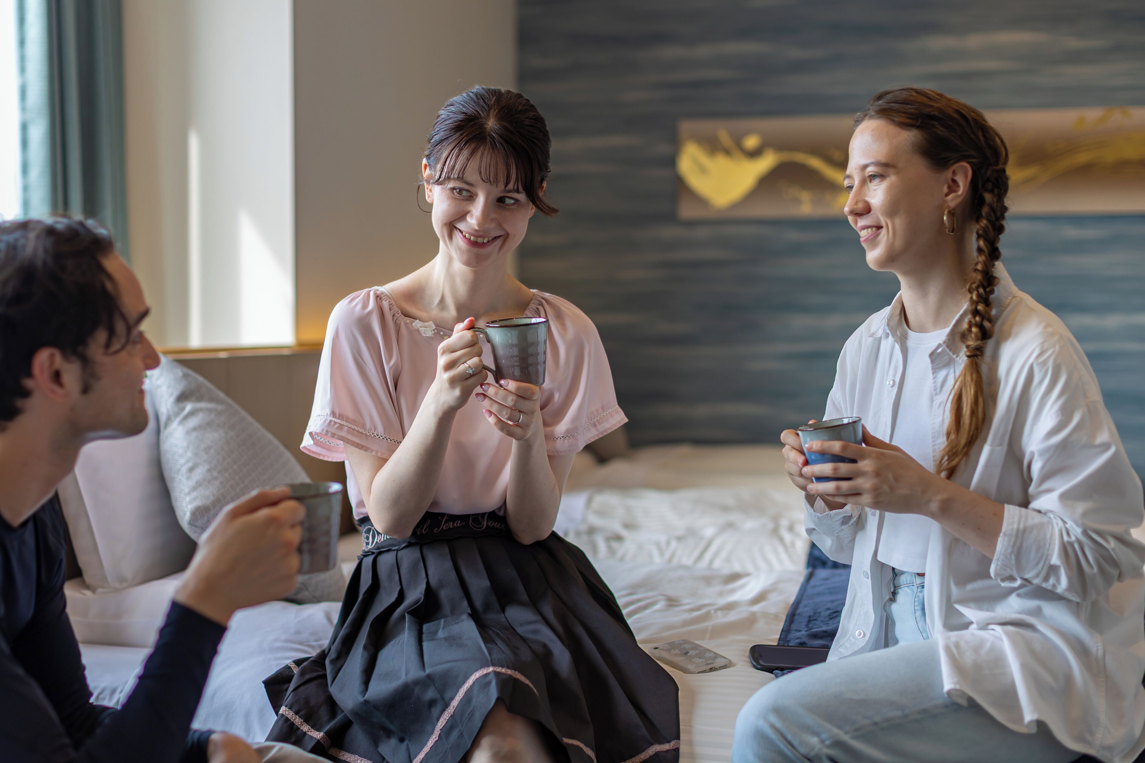 Tres personas sentadas en una cama en una habitación de diseño moderno, sosteniendo tazas.