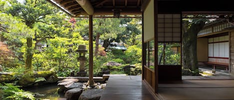 A traditional Japanese garden with a wooden walkway, koi pond, and various trees and rocks.