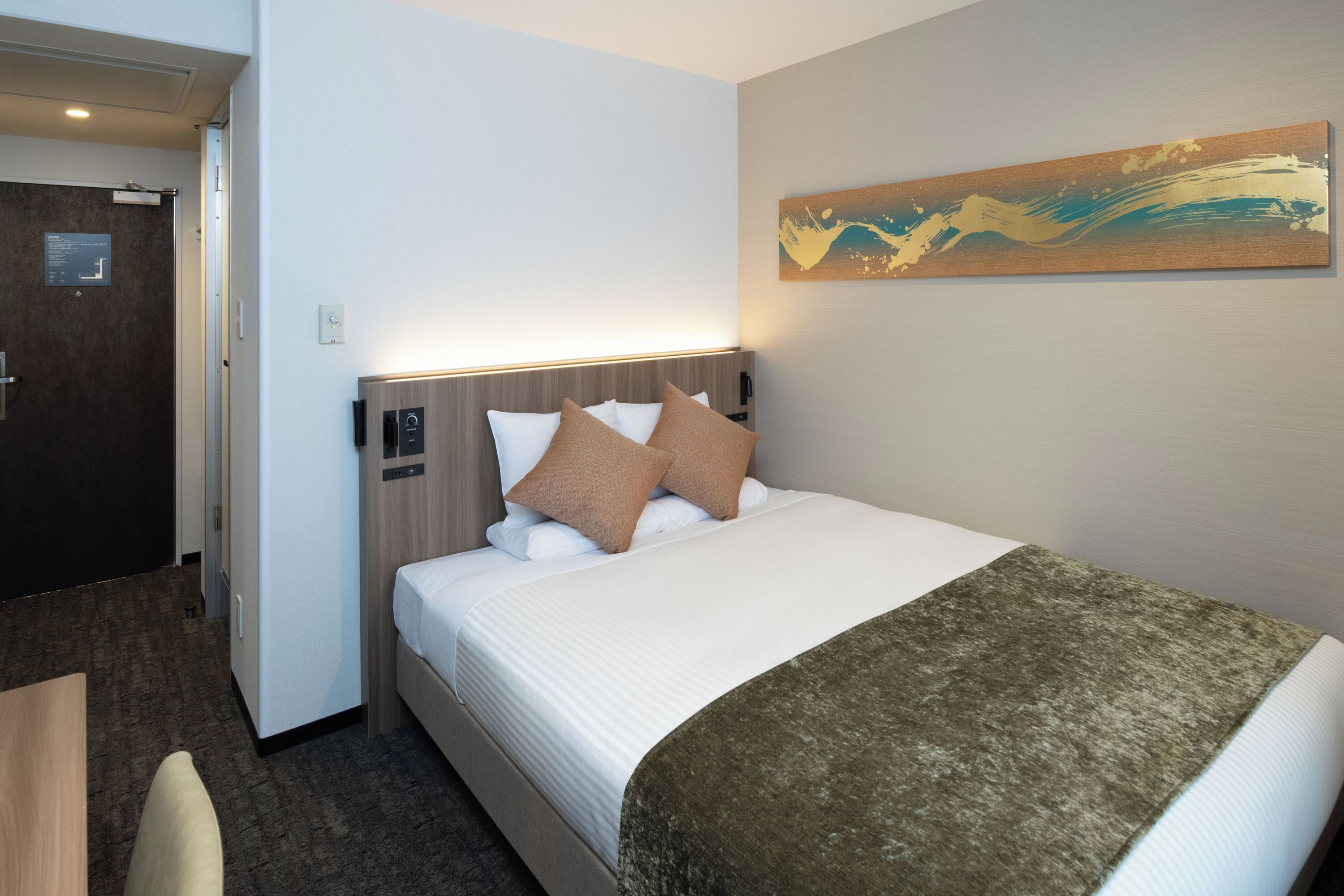 A hotel room with a bed, a desk, and a door.