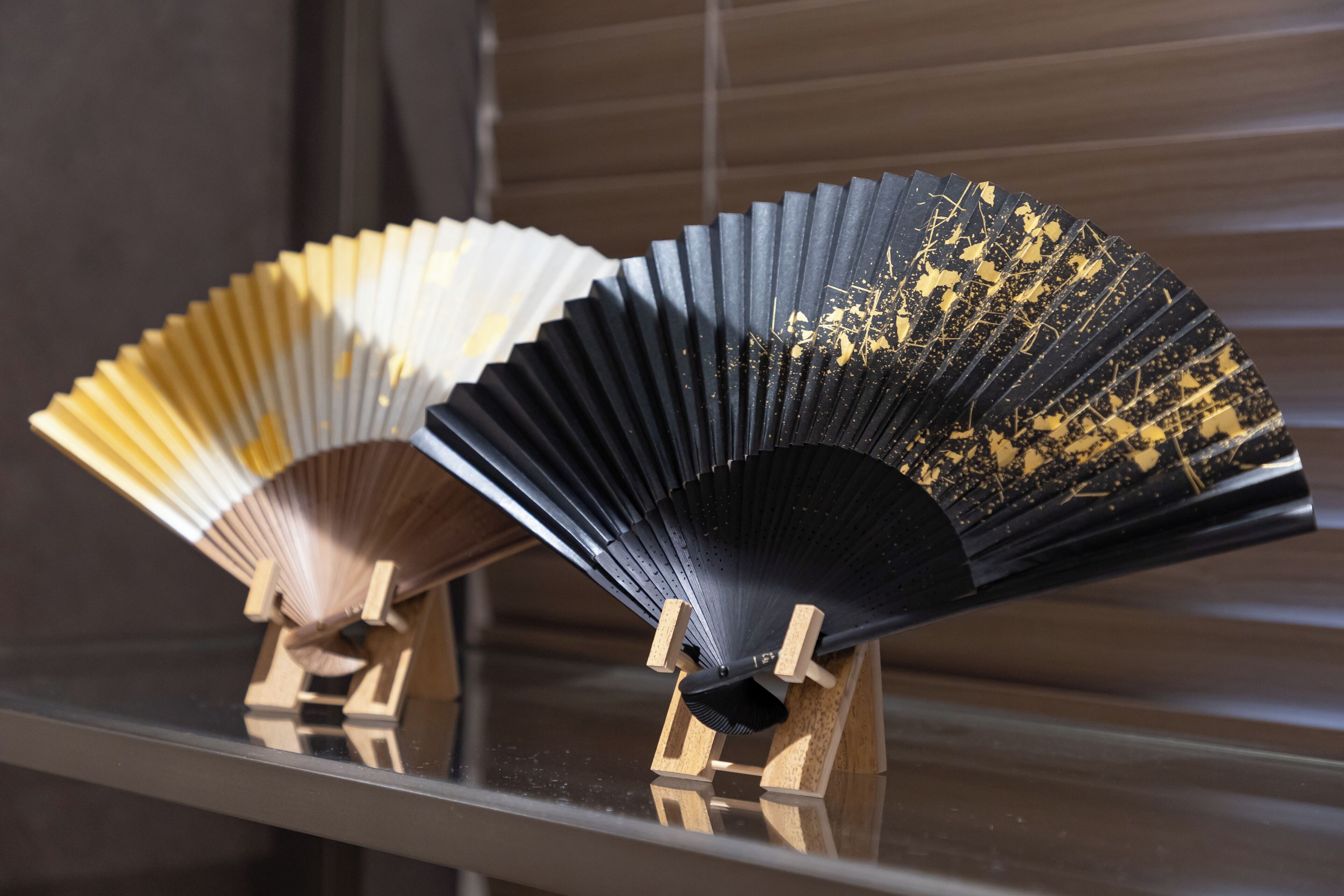 Dos ventiladores con soportes de madera sobre una superficie reflectante.