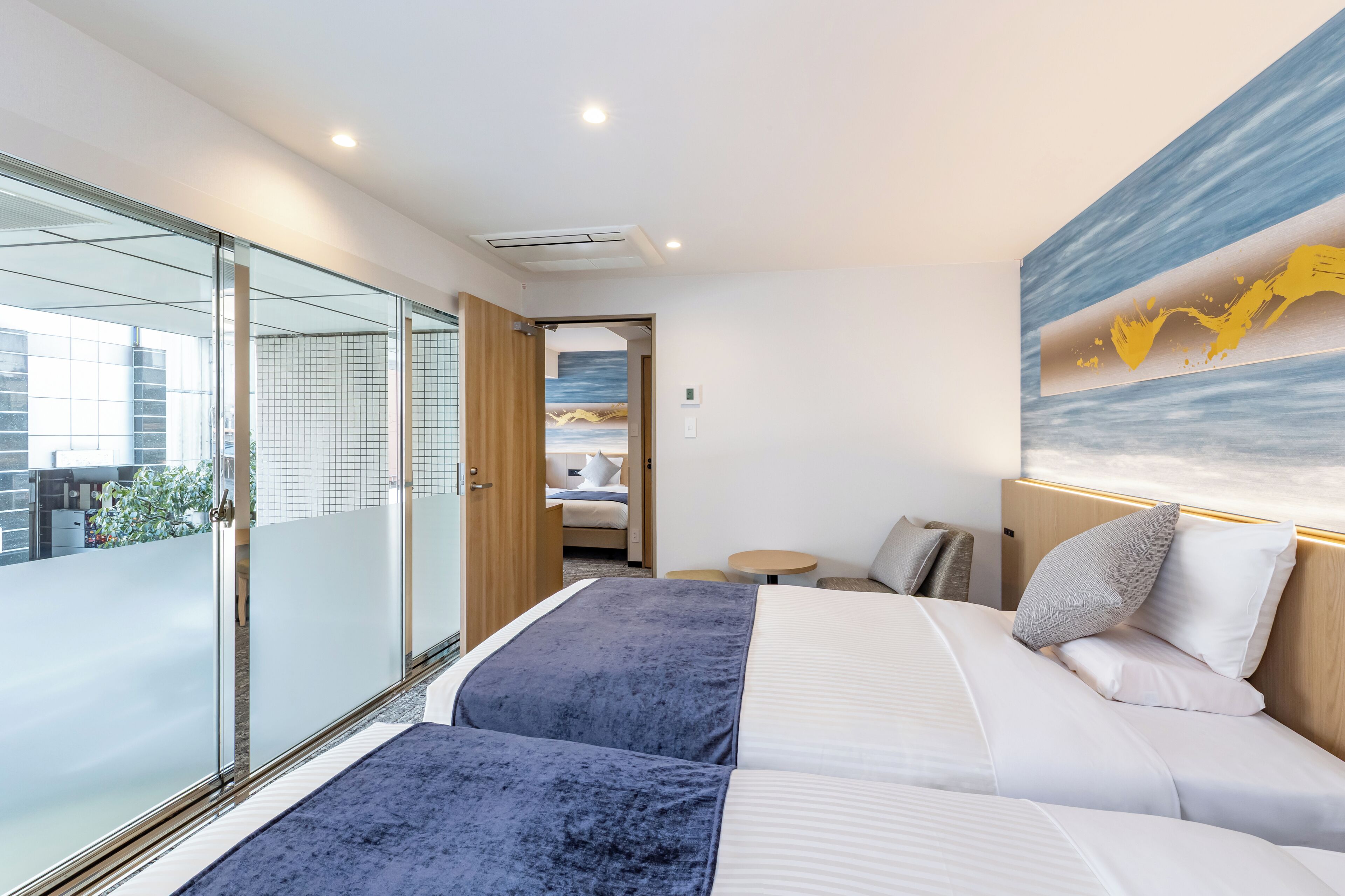 Una habitación de hotel moderna con una cama grande, una puerta de vidrio que da a un balcón y un cuadro en la pared.