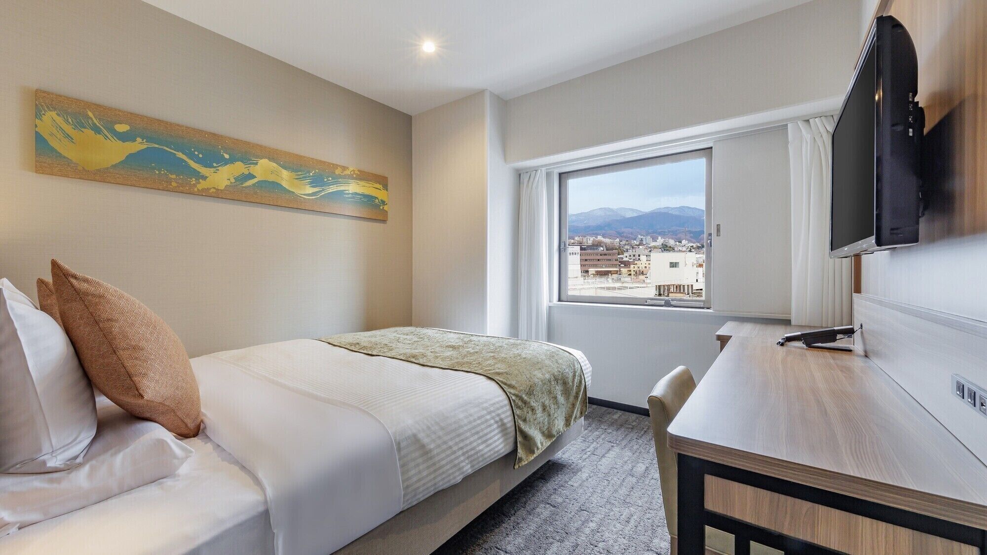 A hotel room with a bed, a desk, a TV, a window with a city view, and a painting on the wall.