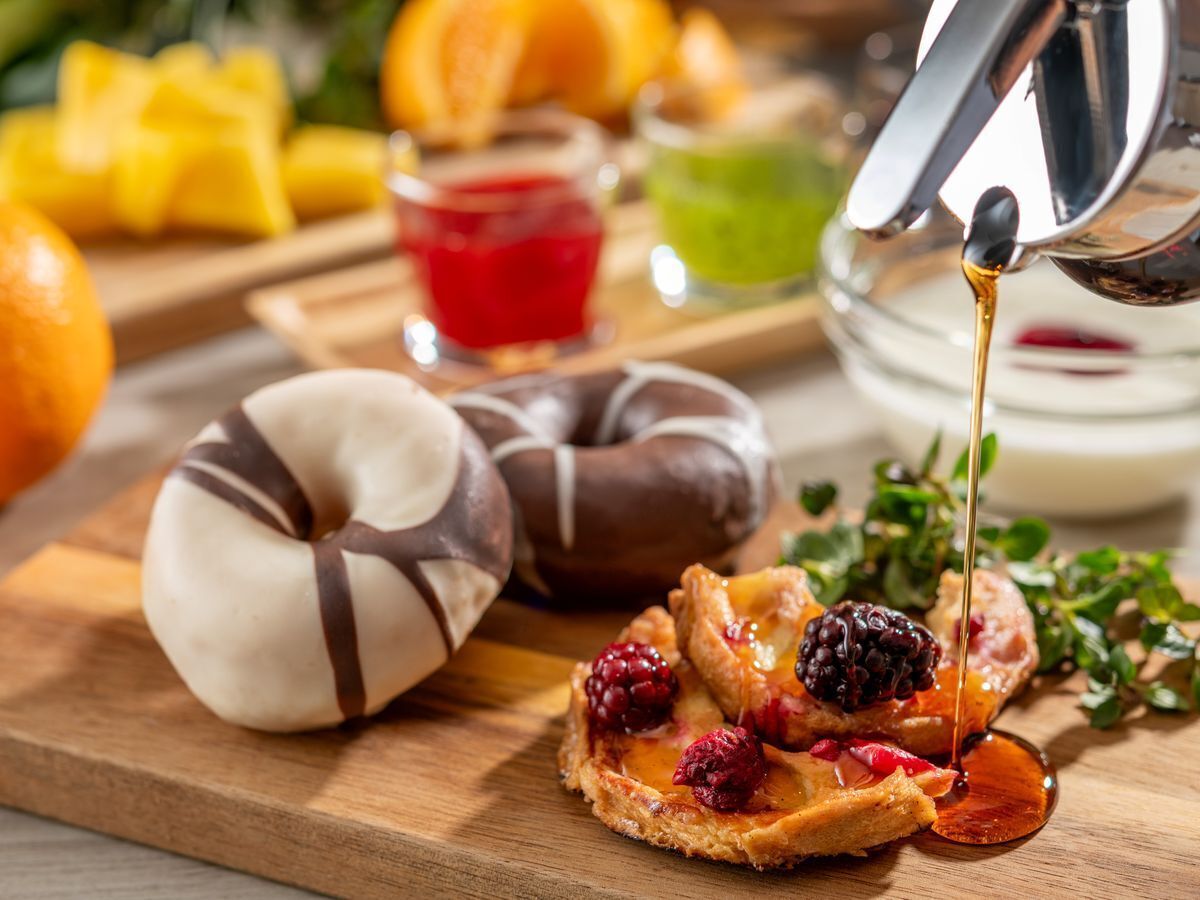 A wooden board with pastries, including a donut and a tart with berries, and a glass of red liquid.