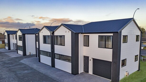 Une rangée de maisons modernes, de plain-pied, dotées de portes de garage et d’un toit plat.