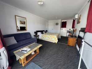 A compact hotel room with a bed, a sofa, a small table, a desk, and a kitchenette.