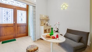 Ein gemütliches Zimmer mit Holztür, einem kleinen Tisch mit Vase und Pflanze, einem grauen Sofa und einer dekorativen Leuchte.