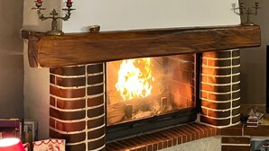 A fireplace with a brick surround and a wooden mantel, featuring a lit fire.