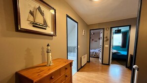 A hallway with a wooden dresser, a framed artwork of a sailboat, and a door leading to a bedroom with a bed and a window.
