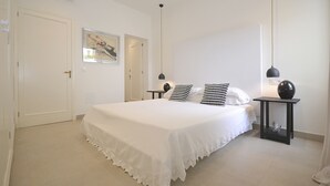 Une chambre à coucher avec un grand lit, une table de chevet avec une lampe, une porte et une œuvre d’art accrochée au mur.