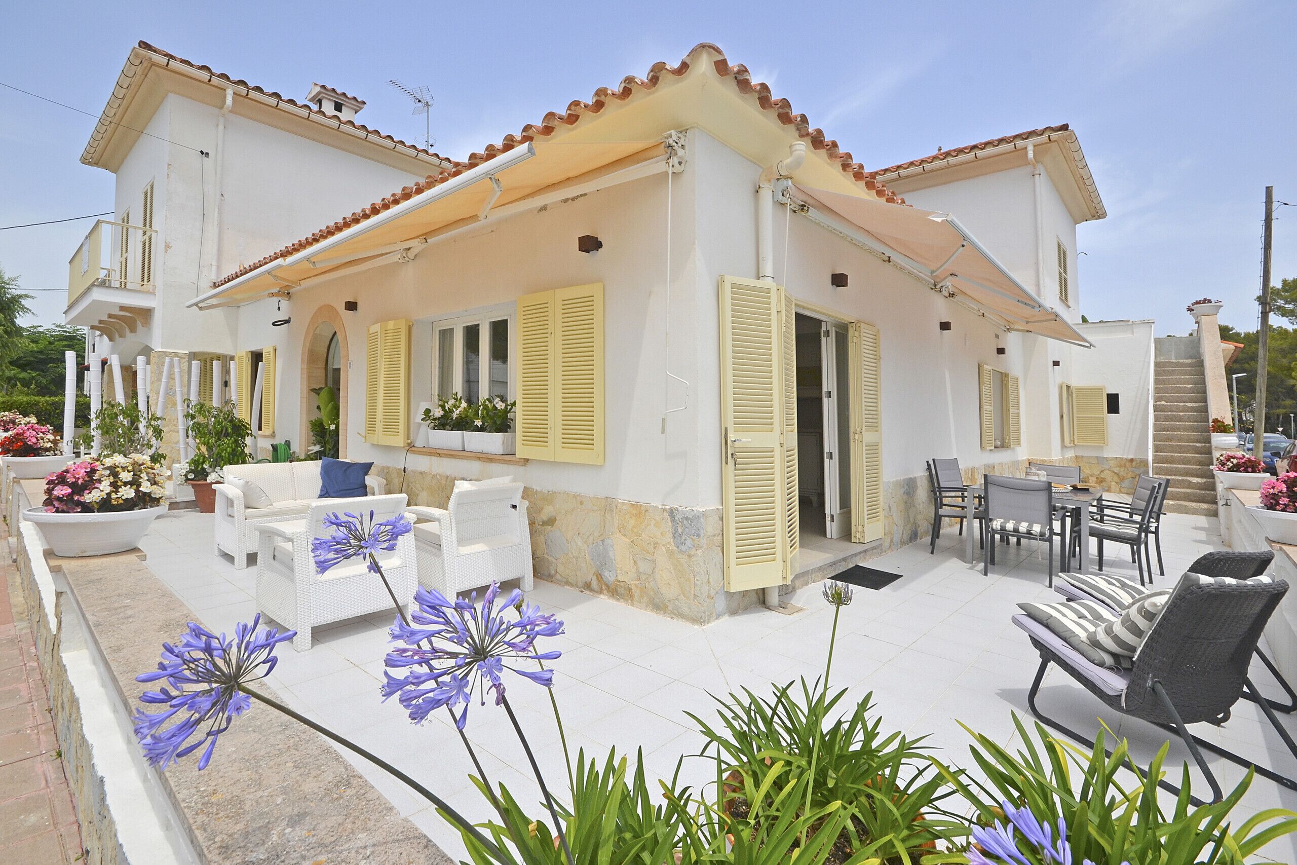 A two-story house with a patio area featuring outdoor furniture, a staircase, and potted plants.