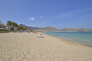 Une plage où des gens se prélassent au soleil, avec des palmiers et des montagnes en arrière-plan.