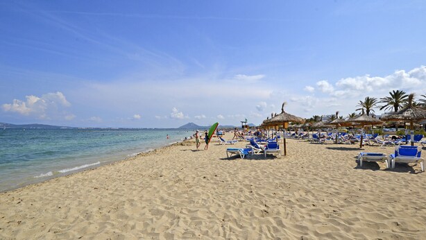 Une plage avec une eau d’un bleu limpide, des chaises longues et des parasols.