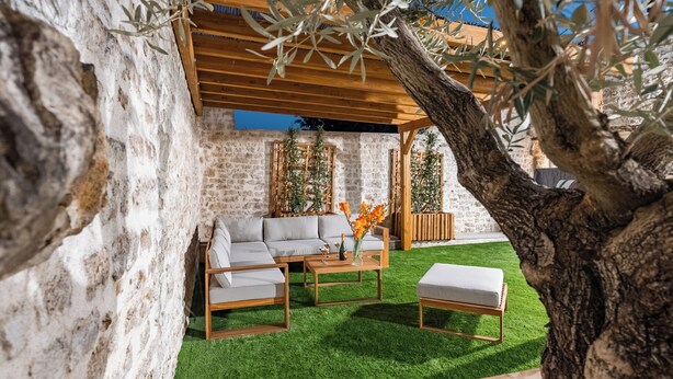 Un espacio exterior acogedor con un banco de madera, un sofá con cojines y una mesa de centro.
