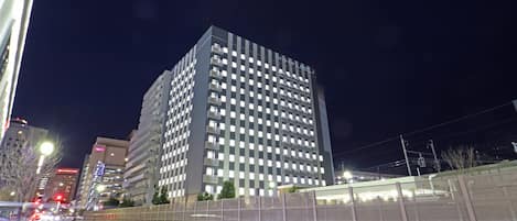 Un edificio de gran altura con varios pisos y balcones, rodeado por un muro de piedra y una cerca de metal.