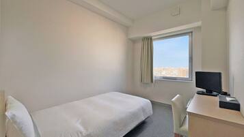 Una habitación pequeña y limpia con una cama individual, un escritorio con una computadora y una ventana con vista a la ciudad.