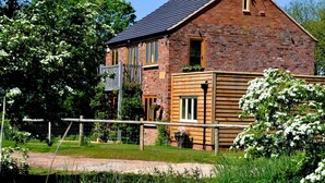 A brick house with a wooden extension, a fenced yard, and blooming white flowers. -  5 Star luxury barn in the Heart of England forest with wood-fired Hot tub. (Great Alne)