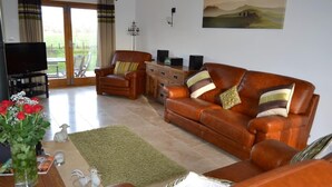 A living room with a brown leather sofa, a wooden coffee table, a TV, and a green rug. -  5 Star luxury barn in the Heart of England forest with wood-fired Hot tub. (Great Alne)