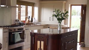 A kitchen with a central island, a stove, oven, and a window with blinds. -  5 Star luxury barn in the Heart of England forest with wood-fired Hot tub. (Great Alne)