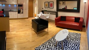 A modern living room with a red sofa, black armchair, and a white coffee table. There is a kitchen in the background with white cabinets and a red countertop. - Apartment - Sleeps 4 - Balcony - Parking - Pets Ok (Hull)
