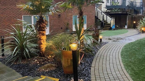 A landscaped garden with a pathway, palm trees, and a brick building with a staircase. - Apartment - Sleeps 4 - Balcony - Parking - Pets Ok (Hull)