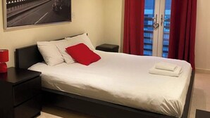 A modern bedroom with a bed, a nightstand, a red lamp, and a window with curtains. - Apartment - Sleeps 4 - Balcony - Parking - Pets Ok (Hull)