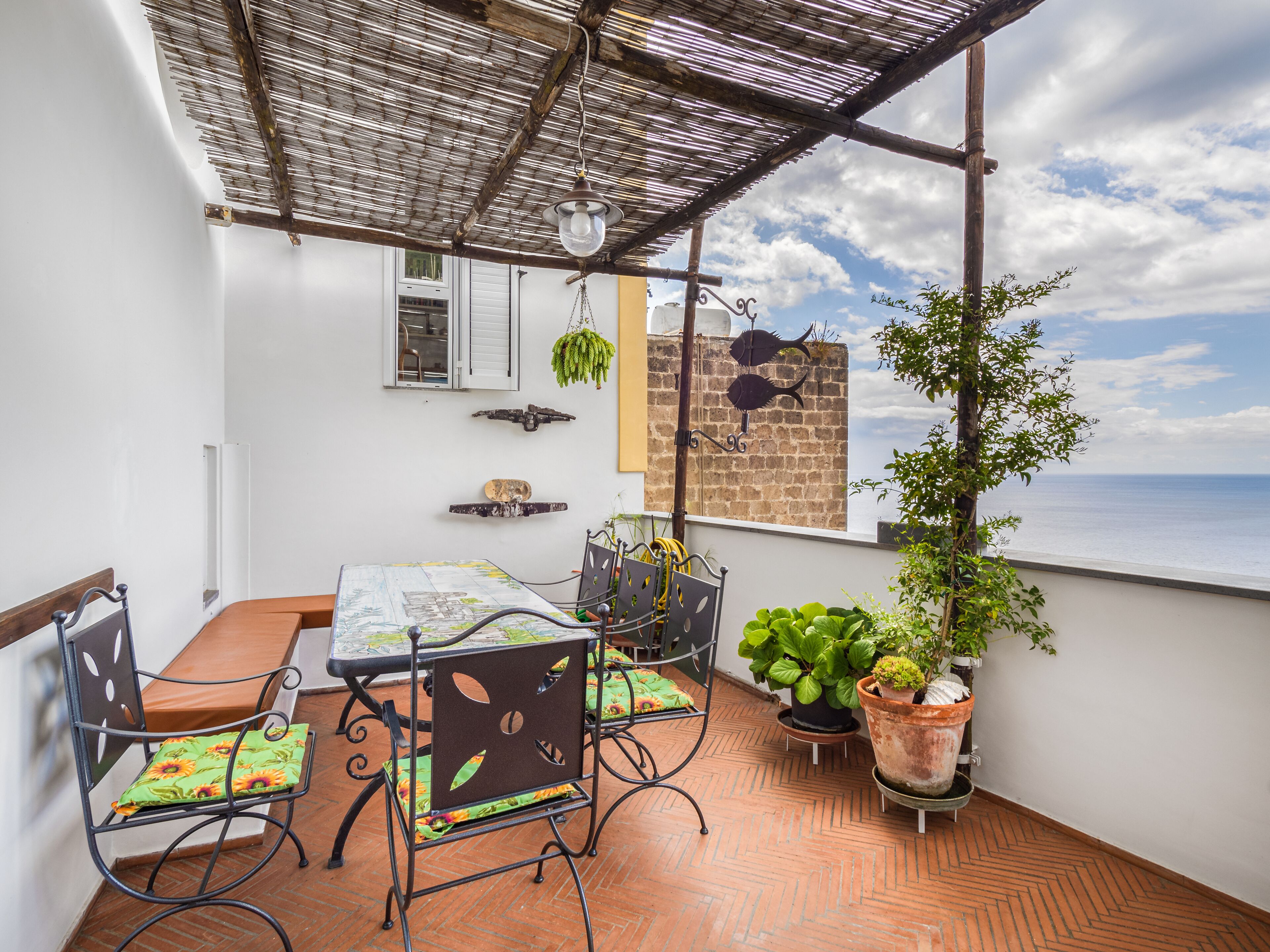 Una terraza con mesa y sillas, plantas en macetas y vista al mar.