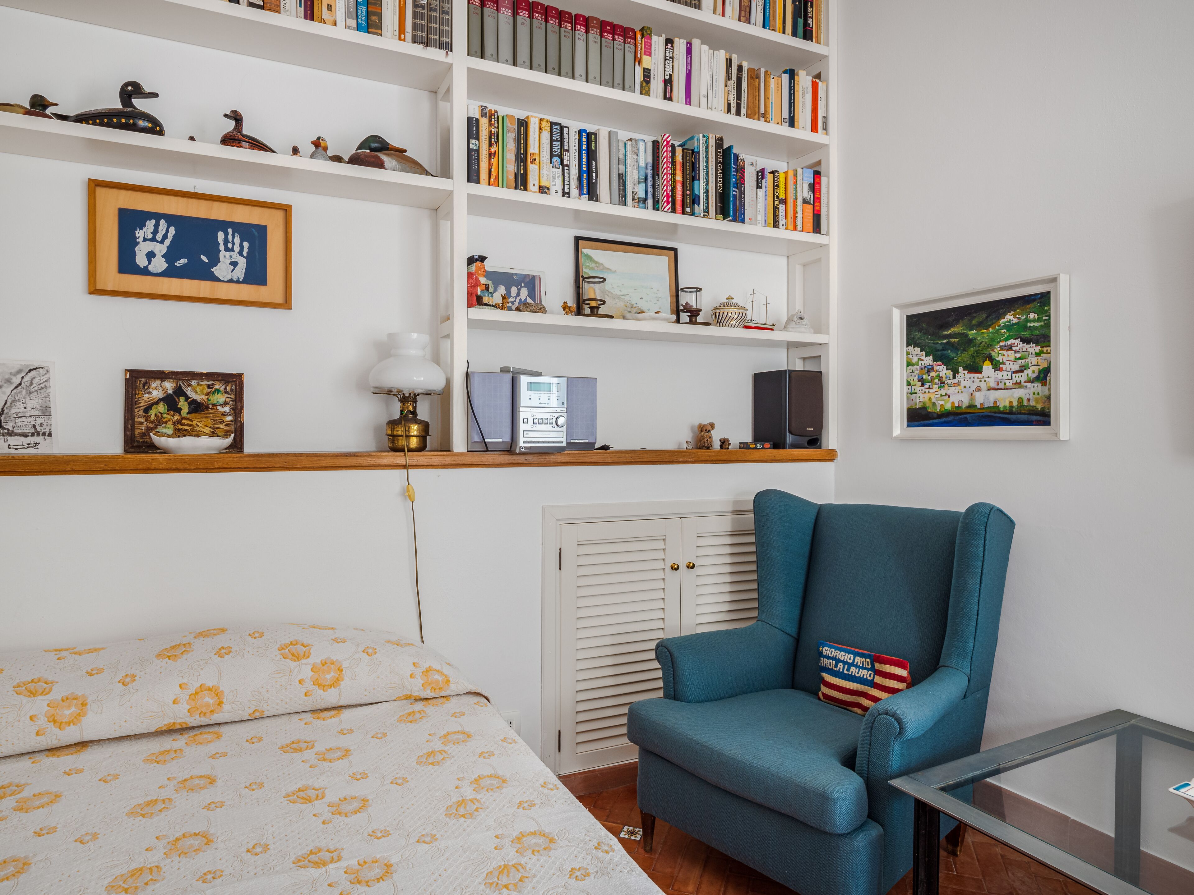 Una habitación con una cama, un sillón azul, una estantería y un cuadro enmarcado en la pared.