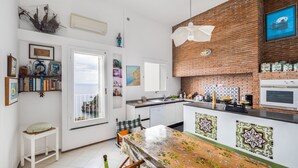 A kitchen with a brick wall, a white refrigerator, and a dining area with a table and chairs. - Casa Lauro (Positano)
