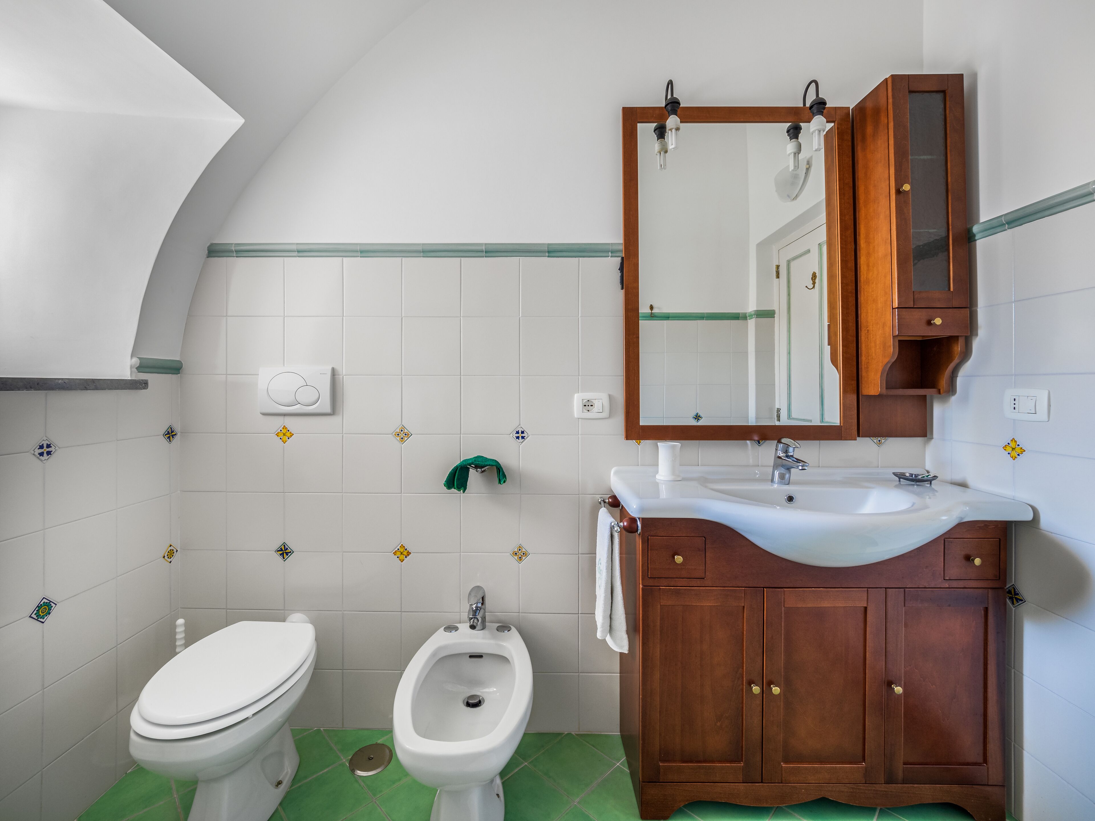 A bathroom with a toilet, bidet, and wooden vanity with a mirror.