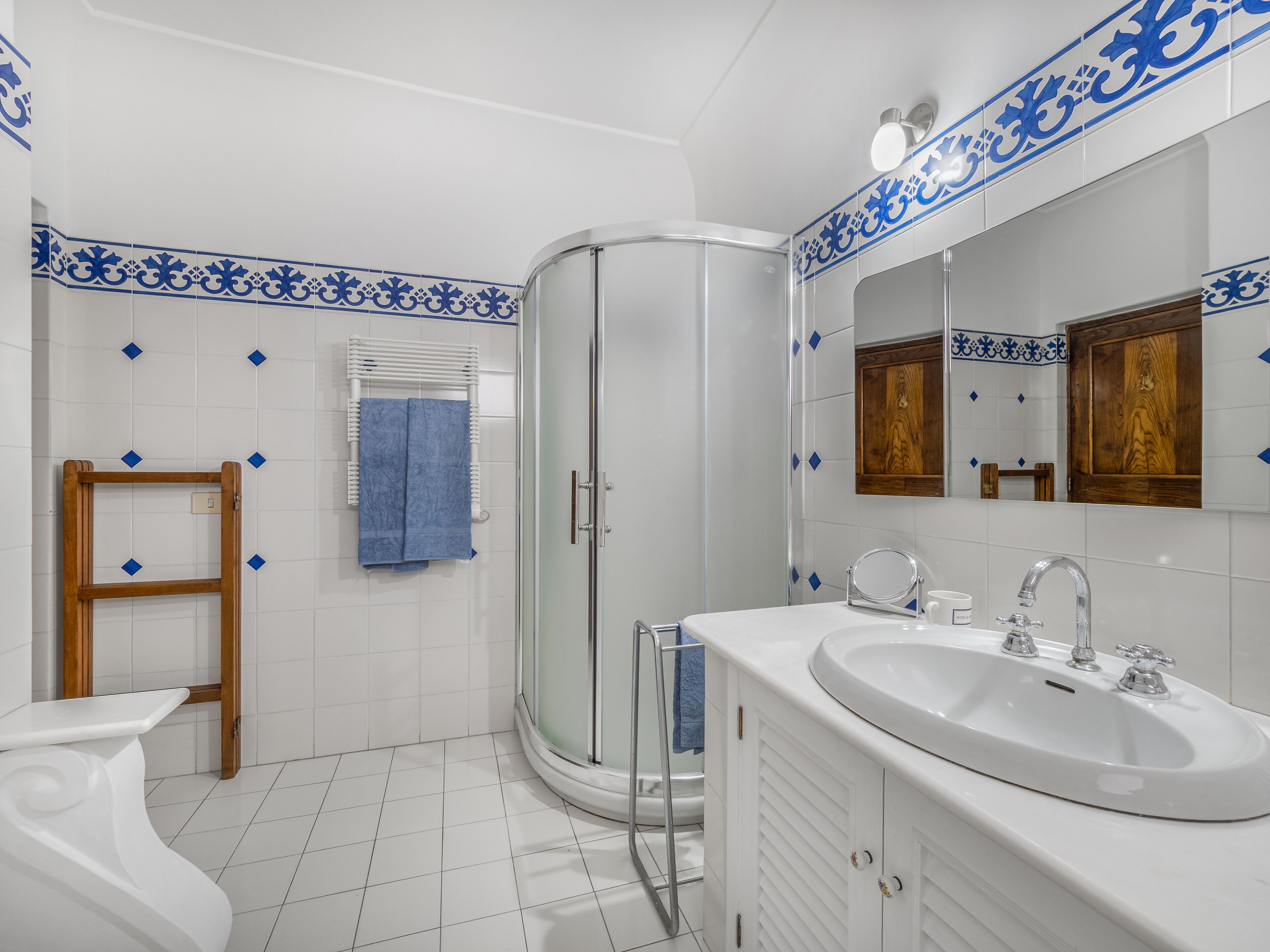 Une salle de bain avec une douche à parois de verre, un lavabo blanc avec un miroir et un porte-serviettes en bois.