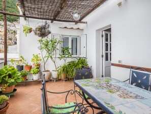 A patio with a tiled table and chairs, surrounded by potted plants and a hanging plant. - Casa Lauro (Positano)
