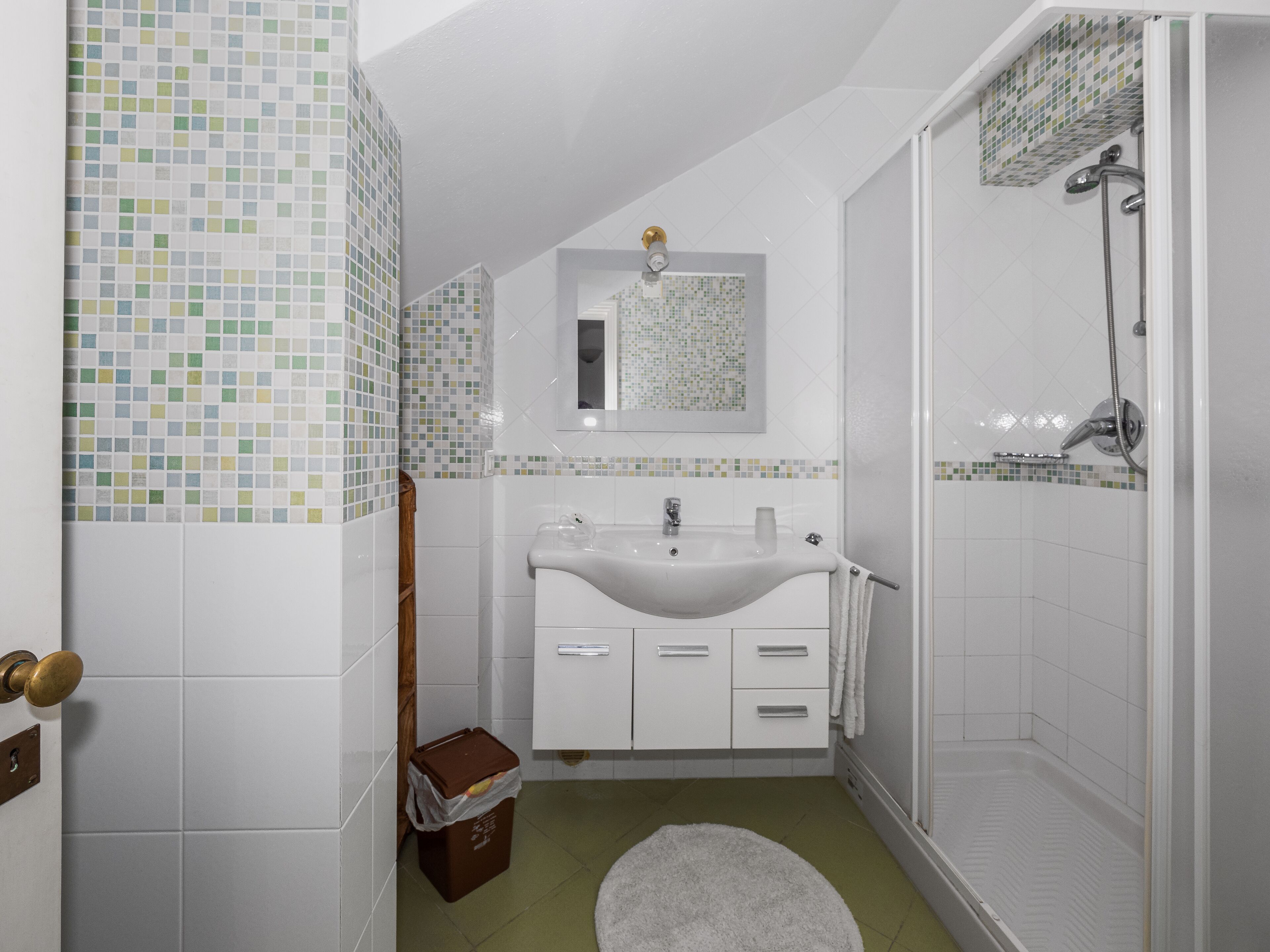 A bathroom with a white sink, a mirror, a shower, and a tiled floor.