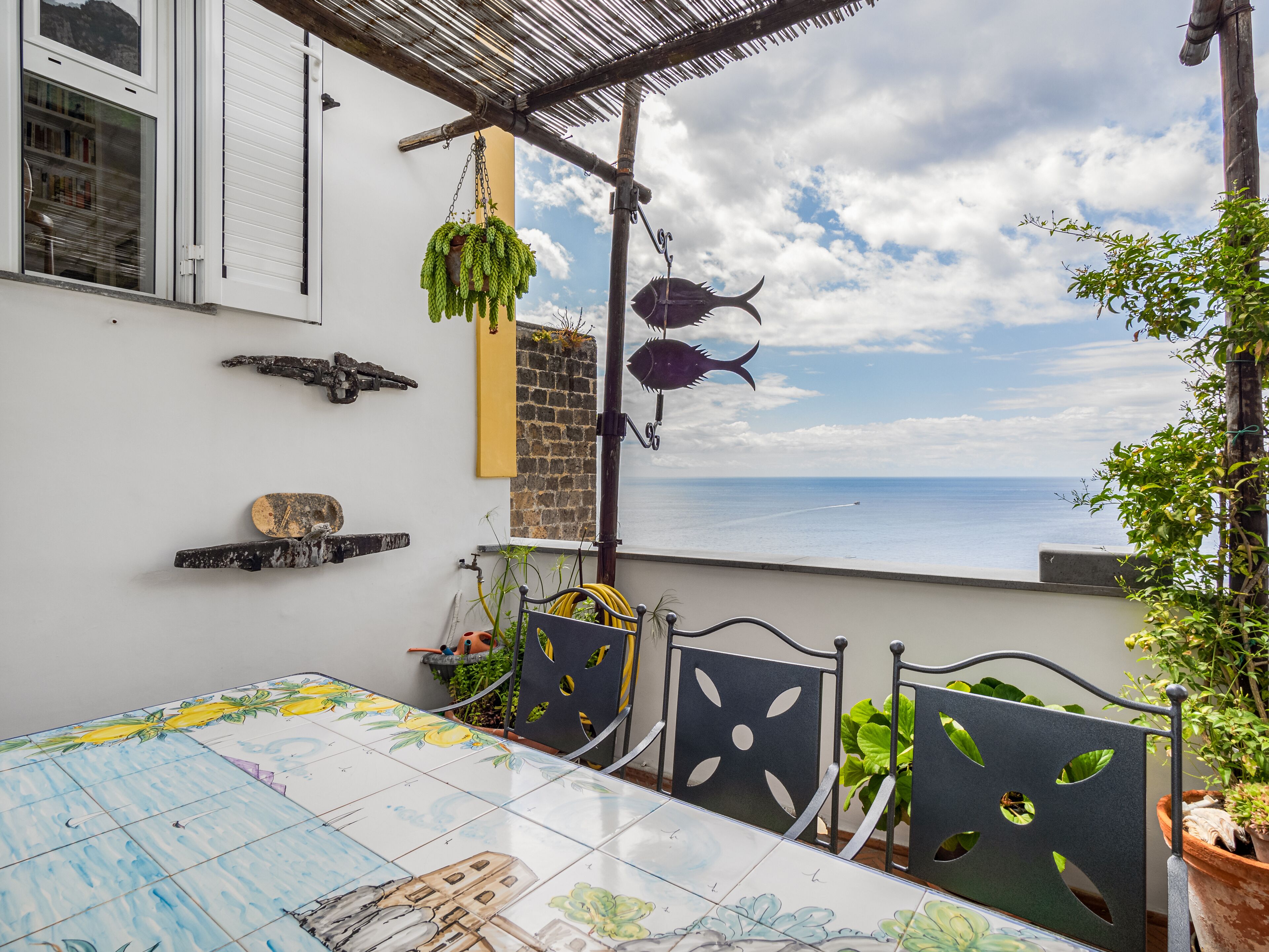 Una terraza con mesa, sillas, plantas colgantes y vista al mar.