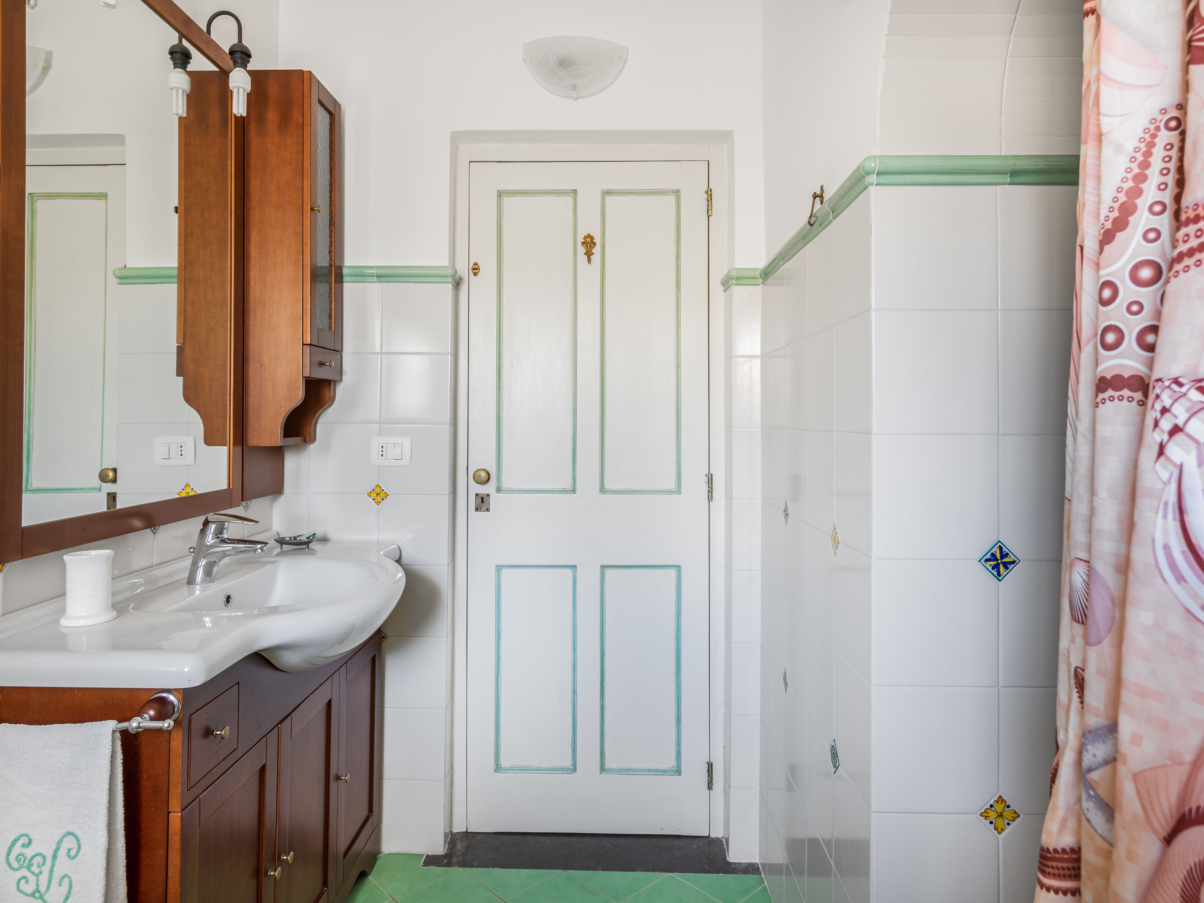 A bathroom with a white sink, wooden cabinets, a mirror, and a door with decorative tiles.